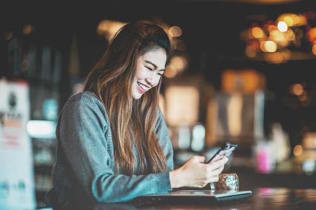 Une femme adulte souriante utilisant un téléphone portable dans un café.