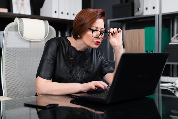 Femme adulte tenant des lunettes et regardant à travers eux dans le moniteur au bureau