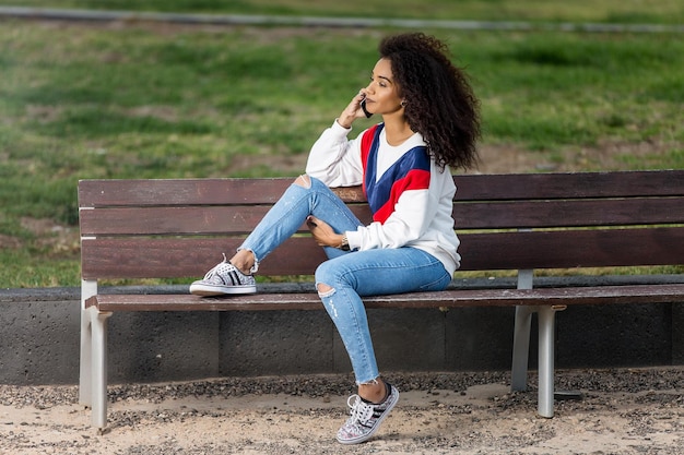 Une femme adulte en train de parler sur son téléphone intelligent alors qu'elle est assise sur un banc dans le parc.