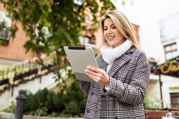 Femme d'affaires adulte plus mince travaillant sur une tablette dans le contexte d'un bâtiment de la ville