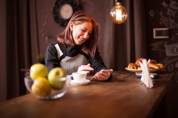 Femme d'affaires adulte riant tout en tenant son téléphone. Détente dans un café