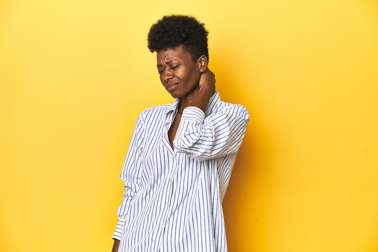 Photo une femme d'affaires africaine en chemise à rayures bleues, fond jaune, souffrant de douleurs au cou en raison du stress.
