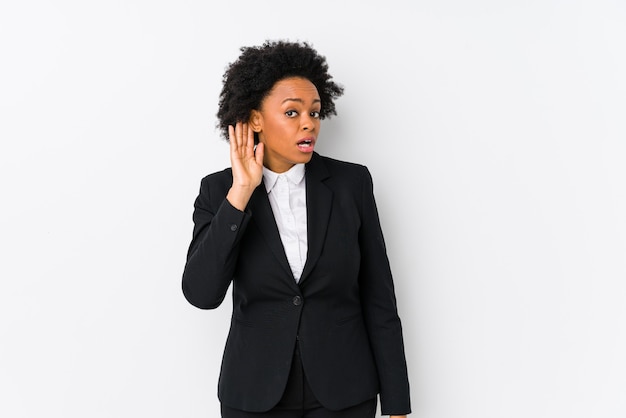 Femme d'affaires afro-américaine d'âge moyen contre un mur blanc isolé en essayant d'écouter un commérage.