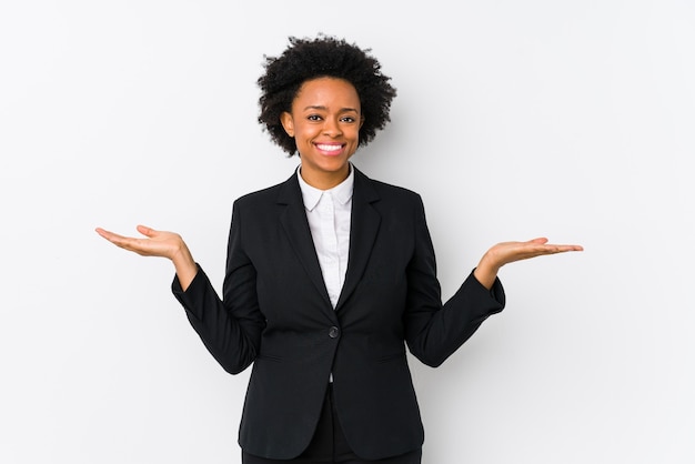 Femme d'affaires afro-américaine d'âge moyen contre un mur blanc isolé fait échelle avec les bras, se sent heureux et confiant.