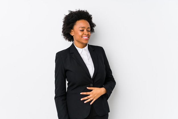 Femme d'affaires afro-américaine d'âge moyen contre un mur blanc isolé touche le ventre, sourit doucement, manger et concept de satisfaction.