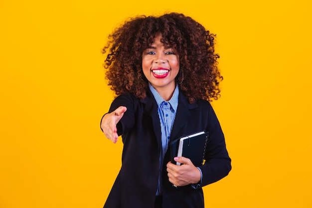 Femme d'affaires afro-américaine d'âge moyen sur fond jaune isolé qui s'étend de la main à la caméra en geste de salutation.