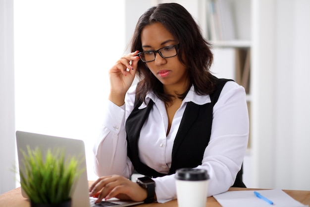 Une femme d'affaires afro-américaine est occupée avec un ordinateur portable au bureau