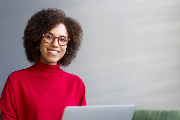 Femme d'affaires afro-américaine portant des lunettes rouges à l'aide d'un ordinateur portable travaillant en ligne dans un bureau moderne