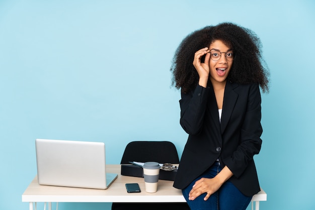 Femme d'affaires afro-américaine travaillant dans son lieu de travail avec des lunettes et surpris