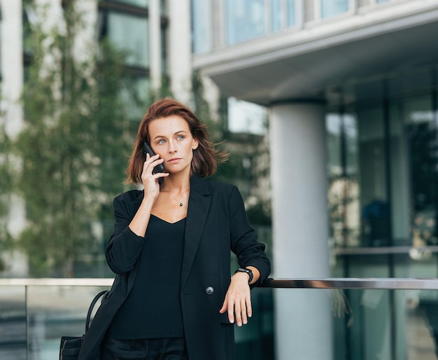 Une femme d'affaires d'âge moyen confiante aux cheveux roux s'appuyant sur la balustrade.