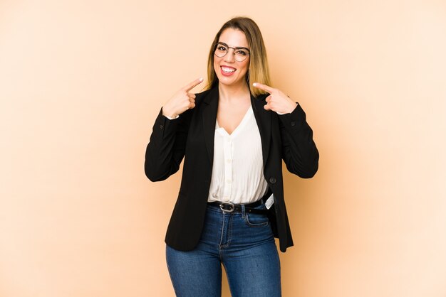 Femme d'affaires d'âge moyen isolé sur des sourires de mur beige, pointant les doigts sur la bouche