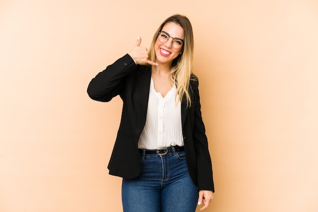 Femme d'affaires d'âge moyen isolée sur beige montrant un geste d'appel de téléphone mobile avec les doigts.