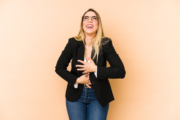 Femme d'affaires d'âge moyen isolée sur fond beige rit joyeusement et s'amuse à garder les mains sur le ventre.