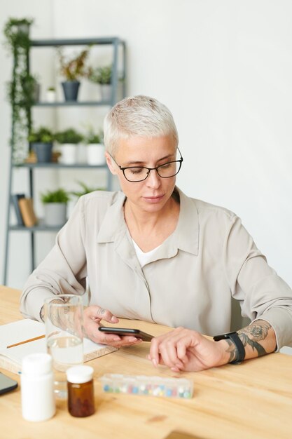 Femme d'affaires d'âge moyen sérieuse dans les lunettes vérifiant l'heure de quart lors de la planification des suppléments je