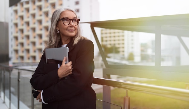 Femme d'affaires âgée avec un ordinateur portable dans les mains sur fond de centre de bureau