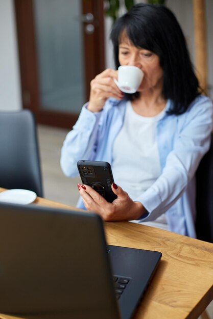 Femme d'affaires âgée se relaxant sur le lieu de travail à l'aide d'un téléphone portable