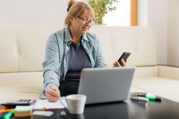 Femme d'affaires âgée travaillant à domicile parlant sur un appel téléphonique mobile en riant en profitant d'une conversation téléphonique à l'aide d'une application en ligne sur un ordinateur portable pour consulter un client