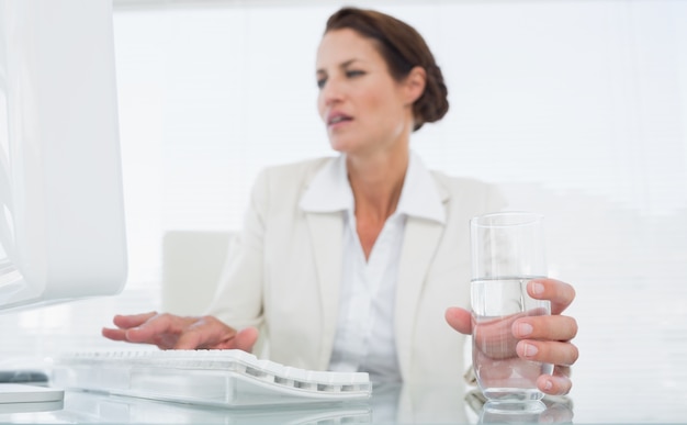 Femme d&#39;affaires à l&#39;aide d&#39;ordinateur tout en tenant un verre d&#39;eau