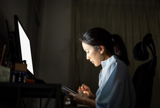 Femme d'affaires à l'aide de téléphone portable tout en travaillant sur l'ordinateur tard dans la nuit.