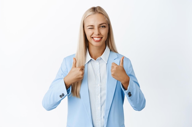 Femme d'affaires ambitieuse montrant les pouces vers le haut et faisant un clin d'œil recommandant ou louant smth bon donner une rétroaction positive debout sur fond blanc