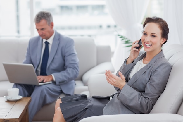 Femme d&#39;affaires appelant pendant que son collègue travaillant sur son ordinateur portable