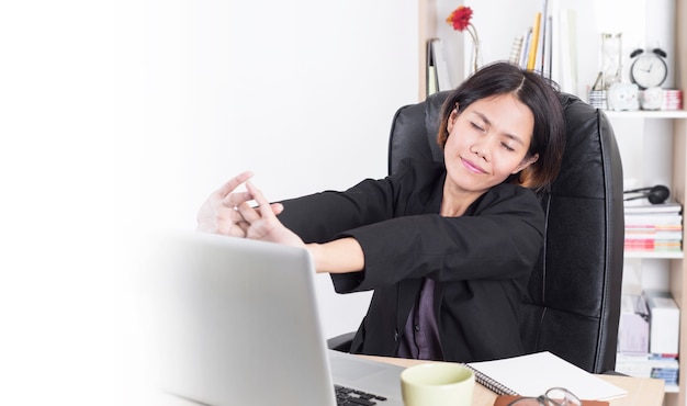 femme d&#39;affaires asiatique assis à la table ordinateur au bureau avec étirement des bras pour se détendre