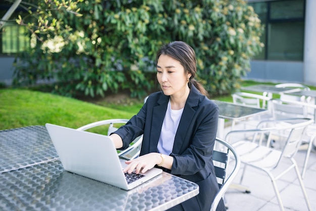 Femme d'affaires asiatique confiante travaillant avec un ordinateur portable en plein air concentré