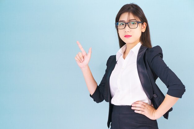 Femme d'affaires asiatique en costume avec le doigt pointé vers le haut sur fond bleu