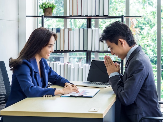 Femme d'affaires asiatique en costume regardant l'homme d'affaires qui salue avec les mains pour payer le respect de style thaï au bureau