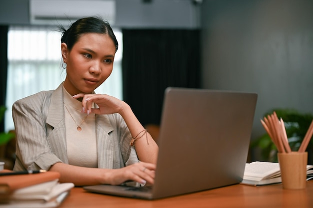 Femme d'affaires asiatique du millénaire professionnelle et confiante travaillant sur ses tâches sur un ordinateur portable