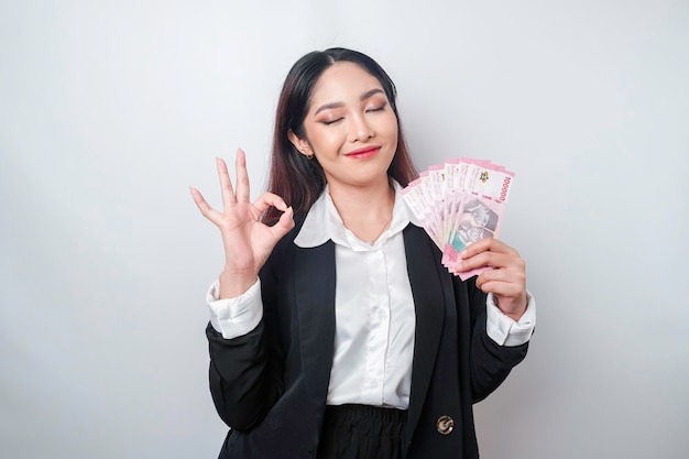 Femme d'affaires asiatique excitée portant un costume noir donnant un geste de la main OK isolé par un fond blanc