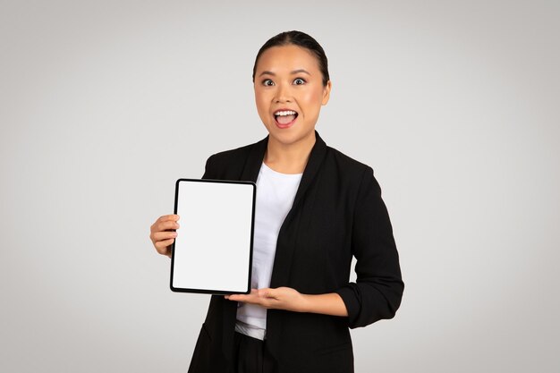 Une femme d'affaires asiatique excitée présentant une tablette avec un écran vide parfait pour les maquettes