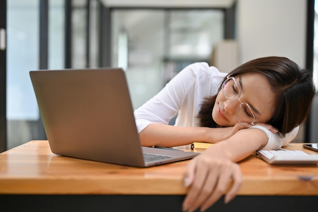 Une femme d'affaires asiatique fatiguée s'endort ou fait une sieste à son bureau