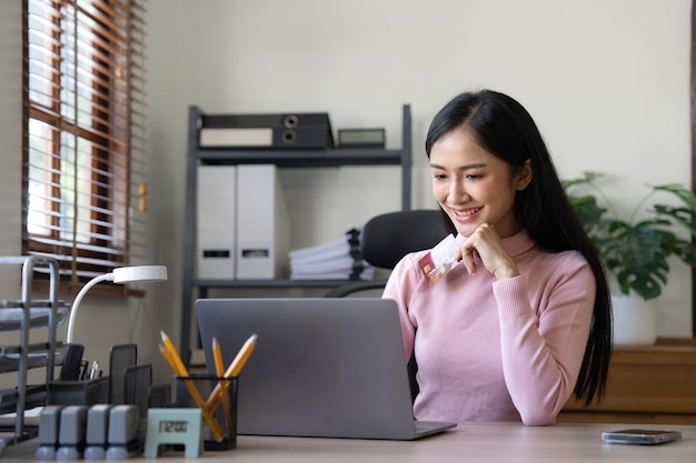 Une femme d'affaires asiatique heureuse paie en ligne à l'aide d'un téléphone portable au bureau