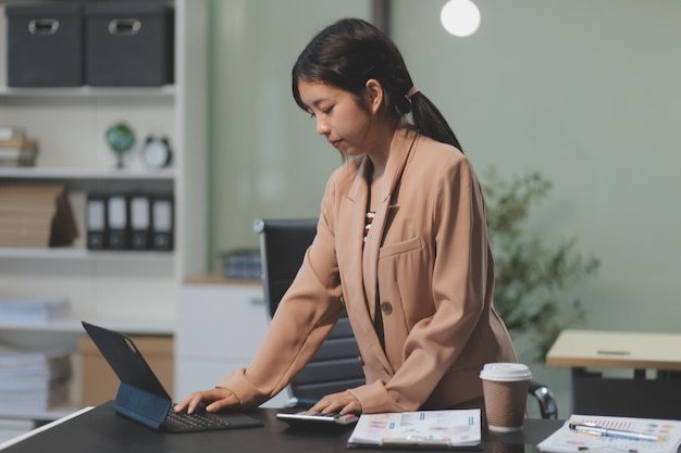 Une femme d'affaires asiatique heureuse travaillant pour son projet et buvant une tasse de café tout en travaillant assise à son bureau