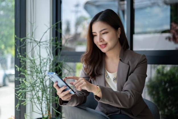 Une femme d'affaires asiatique heureuse utilise son smartphone alors qu'elle est assise dans un café.