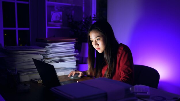 Une femme d'affaires asiatique en ligne travaillant dur jusqu'à tard avec un ordinateur portable à la maison occupée et épuisée par les heures supplémentaires de travail la nuit
