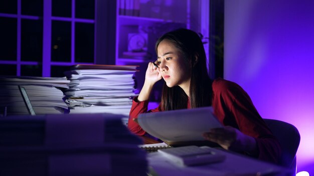 Femme d'affaires asiatique en ligne travaillant dur tard dans la nuit avec un ordinateur portable à la maison. Occupé et épuisé par les heures supplémentaires de travail la nuit.