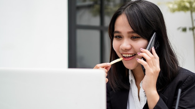 Femme d'affaires asiatique manger et parler sur smartphone au café