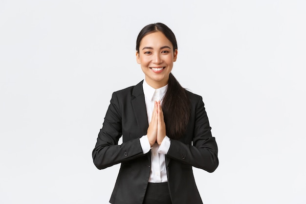 Une femme d'affaires asiatique pleine d'espoir en costume noir s'inclinant poliment et disant namaste, saluant les clients et souriant amicalement. Femme gestionnaire reconnaissante remerciant pour l'aide, étant reconnaissante, appréciant l'aide