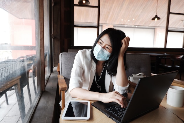 Une femme d'affaires asiatique porte un masque pour prévenir le civid-19 et travailler en ligne avec un ordinateur portable au bureau.