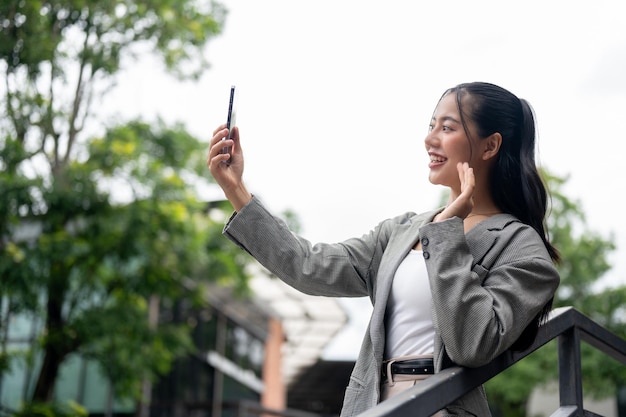 Une femme d'affaires asiatique positive fait un appel vidéo sur son smartphone alors qu'elle se tient à l'extérieur.