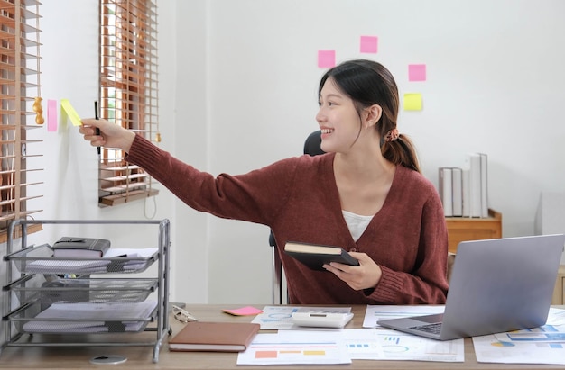 Femme d'affaires asiatique prenant note sur pense-bête Jolie fille travaillant avec un ordinateur portable