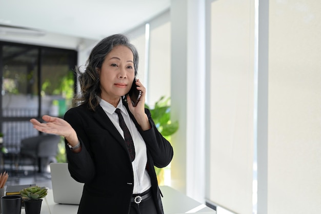 Femme d'affaires asiatique professionnelle âgée parlant au téléphone avec son partenaire commercial au bureau