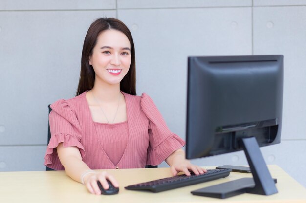 Une femme d'affaires asiatique professionnelle qui porte une robe rose travaille pendant qu'elle est assise au bureau en train de taper.