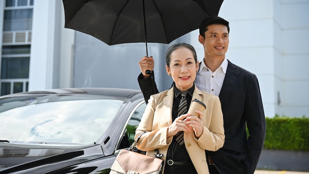 Femme d'affaires asiatique prospère avec un beau garde du corps masculin sous le parapluie