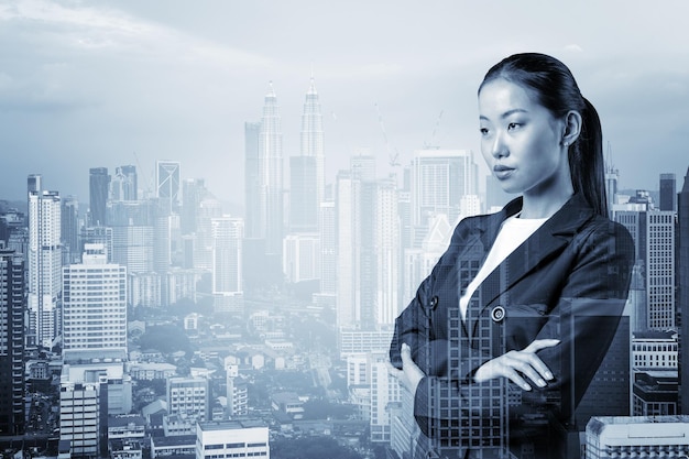 Une femme d'affaires asiatique prospère en costume dans les bras croisés pose le paysage urbain de Kuala Lumpur Le concept de femme dans les gratte-ciel de KL Double exposition