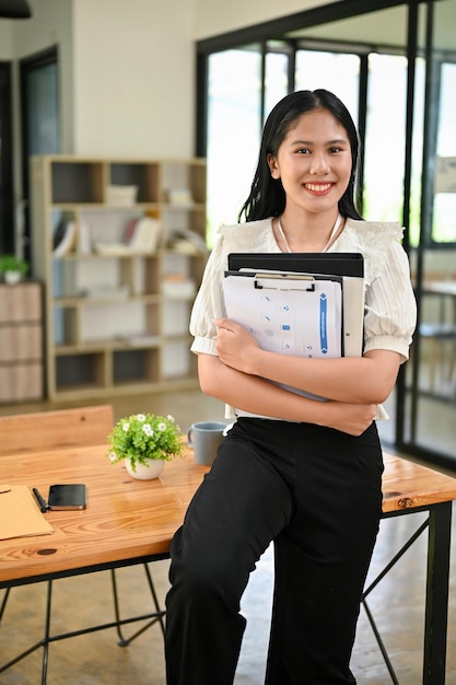 Une femme d'affaires asiatique prospère se tient dans son bureau avec des dossiers de documents dans ses mains
