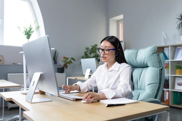 Femme d'affaires asiatique prospère travaillant avec un ordinateur dans un bureau moderne réfléchie et concentrée