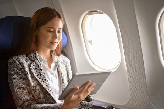 Femme d'affaires asiatique prospère utilisant une tablette pour lire un article d'affaires pendant un vol